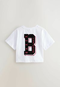 Bílý, zkrácený bavlněný tričko s velkým černým "B" a růžovými akcenty a nápisem "BAKER FOR EVER" v tučném sportovním písmu na zadní straně.