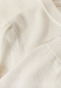Pull en maille blanche avec une texture lisse, un col côtelé et des coutures sur les manches, mettant en valeur un éclat doux et subtil sur le tissu.