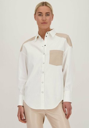Witte button-up shirt met beige schouderaccenten en borstzak. Gladde stof, ontspannen pasvorm en gebogen zoom. Zilveren knopdetails.