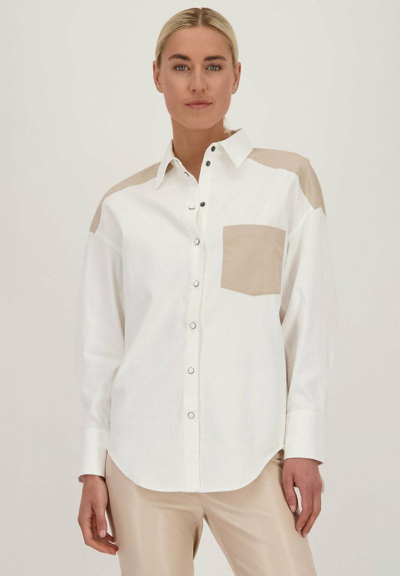 Witte button-up shirt met beige schouderaccenten en borstzak. Gladde stof, ontspannen pasvorm en gebogen zoom. Zilveren knopdetails.