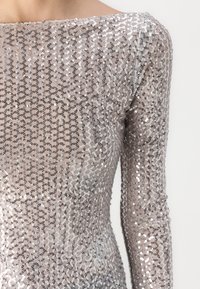 Μπλουζάκι με μακριά μανίκια από διάφανο ύφασμα με σχέδιο από ασημί και μαύρες πούλιες, διαθέτοντας λαιμόκοψη bateau και εφαρμοστή σιλουέτα.