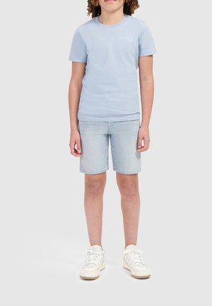 Lichtblauw katoenen t-shirt met "BALLIN" logo, gecombineerd met lichtdenim korte broek tot de knie en witte sneakers met beige accenten.