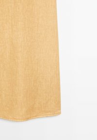 Gros plan sur la partie inférieure d'une jupe en lin beige avec des coutures visibles sur fond blanc.