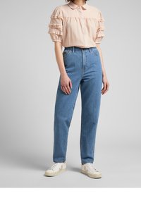 Blusa leggera rosa chiaro con volant e maniche corte, abbinata a jeans dritti azzurri a vita alta e sneakers bianche.