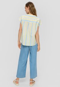 Chemise légère à manches courtes avec des rayures horizontales bleues et jaunes. Associée à un pantalon en denim bleu clair large et des sandales beiges.