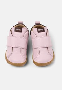 Zapatos de cuero rosa con cierre de velcro, diseñados con una puntera redondeada y detalles marrones en el talón. Suela de goma para mayor tracción.