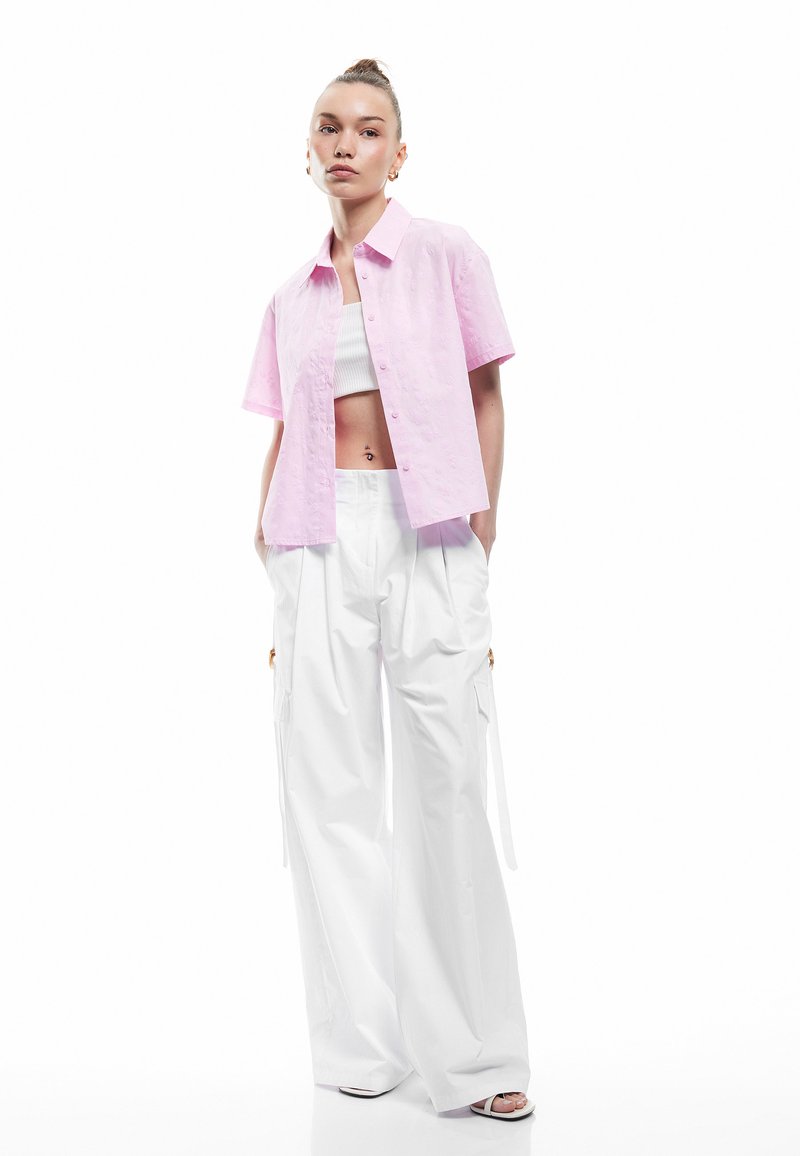 Kortärmad ljusrosa button-up skjorta med en texturerad yta, matchad med vita vida byxor som har sidofickor och snörning.