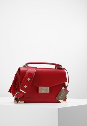 Rote Lederhandtasche mit Tragegriff oben, verstellbarem Schulterriemen, goldfarbenem Drehverschluss, Eckschutz und einem Anhänger mit der Aufschrift „JUST KEEP MY BAG."