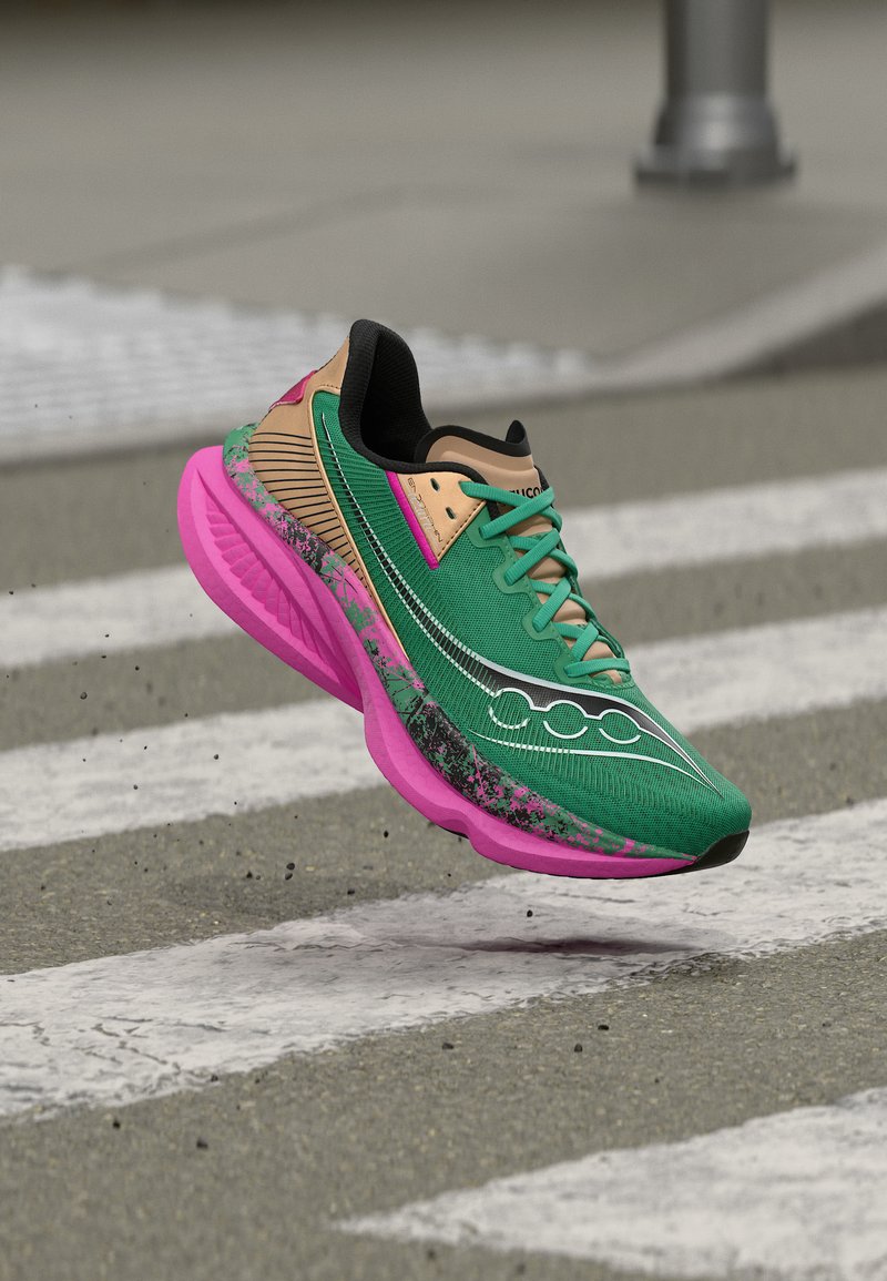 Chaussure de course verte et beige avec semelle rose en l'air au-dessus d'un passage piéton sur une rue avec un arrière-plan flou.