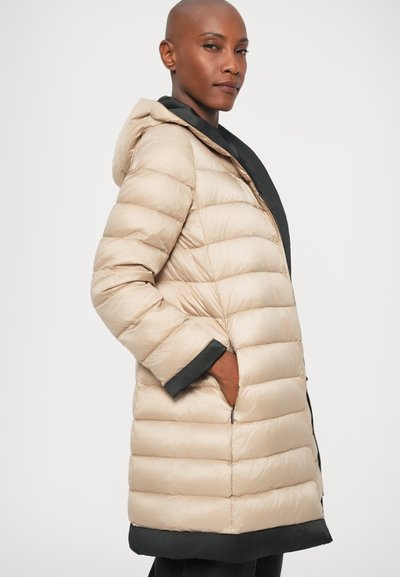 Cappotto imbottito beige con cuciture orizzontali, dettagli neri sui polsini e sull'orlo, dotato di cappuccio e tasche laterali. Materiale liscio e leggero.