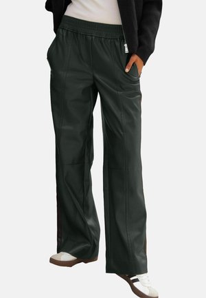 Black wide-leg pants with elastic waistband worn with white sneakers and a black jacket, hands in pockets, on a white background.