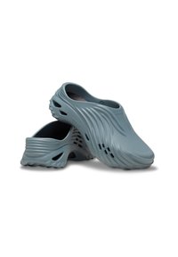 Helle blaue Clogs mit einer strukturierten, gewellten Oberfläche. Hergestellt aus flexiblem Material, mit Belüftungsöffnungen und einem abgerundeten Zehenbereich.