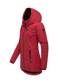 Giacca rossa con cappuccio, chiusura a zip, cordini regolabili, dettagli neri, due tasche con zip e una parte posteriore più lunga.