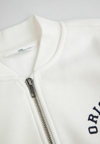 Biały rozpinany sweatshirt z półkołnierzem, z metalowym zamkiem w kolorze srebrnym oraz granatowym haftowanym napisem. Gładka faktura, ściągacze na kołnierzu.