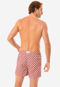 Costume da bagno a righe rosso e crema con vita elastica, caratterizzato da un design geometrico e una piccola etichetta con logo sul retro.