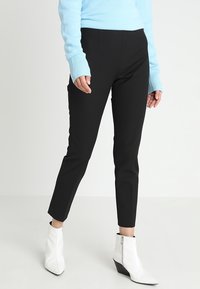 Zwarte getailleerde broek met een gladde textuur en enkel lengte, gecombineerd met witte ritsen enkelboots en een lichtblauwe trui.