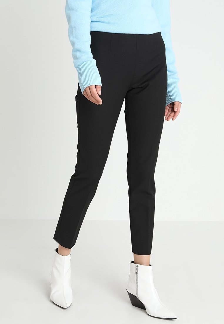 Zwarte getailleerde broek met een gladde textuur en enkel lengte, gecombineerd met witte ritsen enkelboots en een lichtblauwe trui.