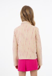 Giacca a righe crema e rosa con una vestibilità rilassata e colletto ripiegato, abbinata a pantaloni corti rosa brillante. Tessuto morbido e testurizzato.