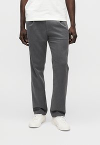 Pantaloni grigi in tessuto strutturato, con taglio diritto e tasche laterali, abbinati a sneakers bianche.