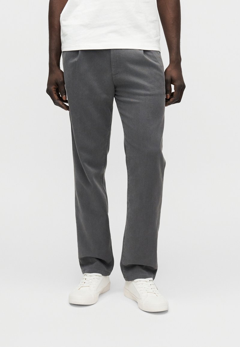 Pantaloni grigi in tessuto strutturato, con taglio diritto e tasche laterali, abbinati a sneakers bianche.