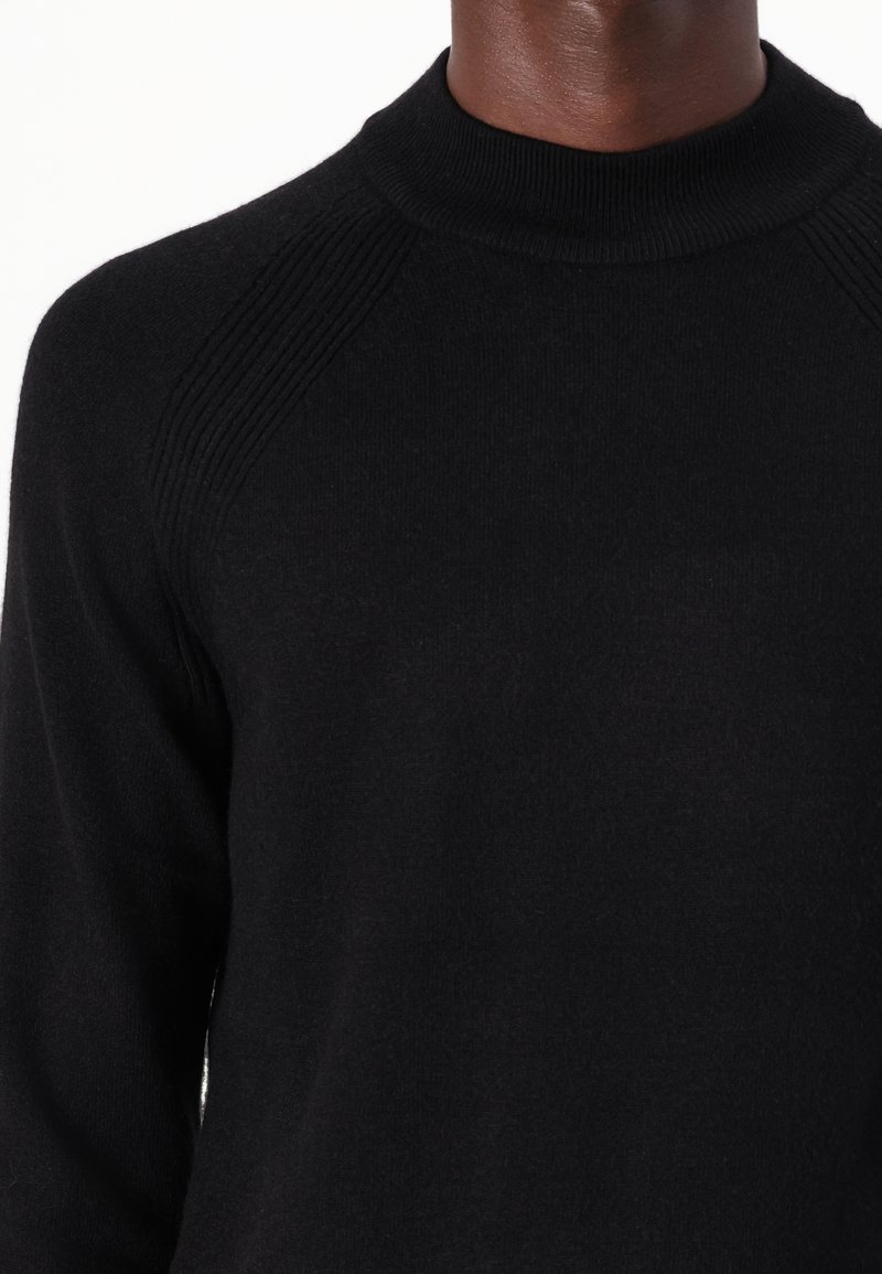 Schwarzer Pullover aus weichem Material, mit hohem Kragen, gerippten Schulterakzenten und figurnaher Passform. Keine sichtbaren Muster oder Logos.