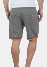 Pantaloni scurți gri din bumbac, cu un elastic la talie, margine portocalie la baza și două buzunare la spate. Textură netedă, design casual.