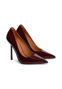 Pár lesklých tmavě červených lodiček s špičatou špičkou a vysokým podpatkem s béžovým vnitřním podšíváním na bílém pozadí.