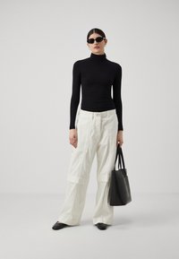 Svart langermet turtleneck, hvite vide cargo-bukser med lommer, svart totebag og svarte spisse sko. Minimalistisk design.