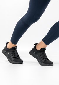 Black athletic shoes with mesh and rubber accents, featuring a low-top design and laces. Worn with dark blue leggings.