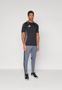 Sort atletisk T-shirt med grå sidepaneler, parret med grå bukser med sorte sidestriber og sorte atletiske sko.