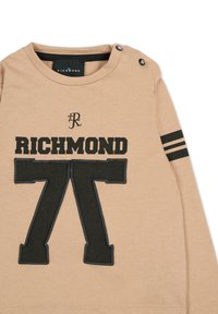Beżowa bluza z czarnym napisem "RICHMOND 77" i dużym czarnym nadrukiem. Zapięcia na guziki na ramieniu oraz paski na rękawach.