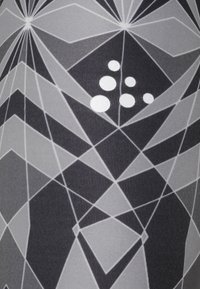 Geometrické legíny s černobílým vzorem, které obsahují úhlové tvary a pět bílých kruhových akcentů na přední straně.