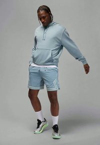 Ανοιχτό μπλε φούτερ με τσέπη μπροστά, σε συνδυασμό με κοντό παντελόνι από δίχτυ που έχει λευκό γεωμετρικό σχέδιο. Αθλητικά παπούτσια με ασημί και πράσινα στοιχεία.