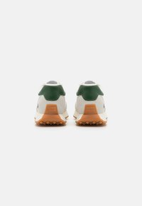 Sneakers con tallone in suede verde, tomaia bianca e suola in gomma arancione. Presentano dettagli testurizzati e un logo del brand in rilievo sul tallone.