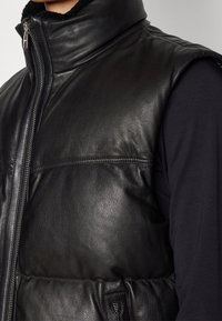 Svart läderväst med hög krage, med en slät textur, dragkedjestängning och vadderade detaljer fram. 