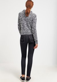 Jeans skinny neri con tasche posteriori caratterizzate da un sottile design di cucitura, abbinati a un maglione grigio lavorato a maglia con un tessuto texture.