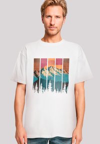 Witte katoenen t-shirt met een grafisch ontwerp van bergen en bomen in turquoise, oranje en bruine strepen. Korte mouwen met een ontspannen pasvorm.