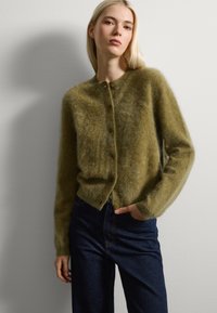 Cardigan verde esponjoso hecho de una tela suave, con un escote redondo, cierre de botones y puños acanalados, combinado con jeans oscuros de cintura alta.