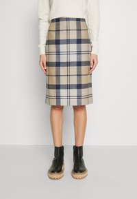 Wollen midi-rok in ruitpatroon met beige, marineblauw en wit, voorzien van een aangesloten taille. Gecombineerd met zwarte enkellaarzen en een lichte trui.