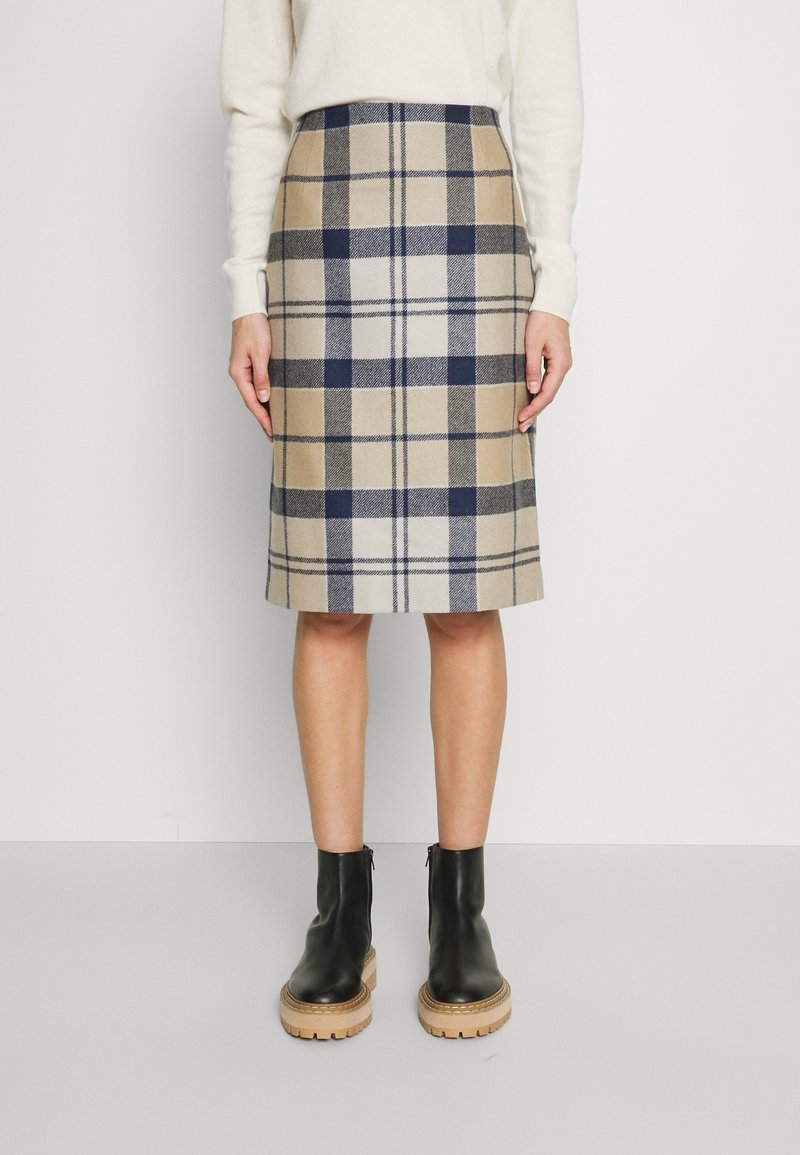 Wollen midi-rok in ruitpatroon met beige, marineblauw en wit, voorzien van een aangesloten taille. Gecombineerd met zwarte enkellaarzen en een lichte trui.