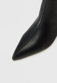 Stivale in pelle nera a punta con texture liscia, dettagli di cucitura discreti e una silhouette elegante. Il design della tomaia è aderente e affusolato.