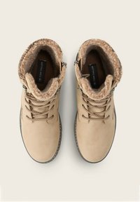 Botas de invierno beige con cordones y forro de pelo, con cremalleras laterales, vistas desde arriba sobre un fondo claro.