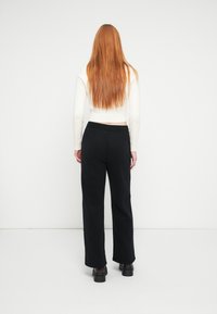 Črne široke hlače z udobnim pasom, kombinirane z belo kratko pulover s pletenim vzorcem, pogled od zadaj.