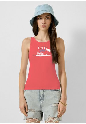 Jeune femme portant un débardeur corail avec un motif de chaises de plage et parasol, un chapeau bob bleu clair et un short en jean déchiré.