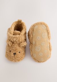 Kamel rjavi copati s poudarkom na medvedjem obrazu, mehko teksturo in oblazinjenim notranjim delom. Podplat ima medvedji vzorec, izbočen na bež podlagi.