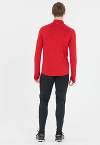 Punainen pitkähihainen paita, jossa on mock neck ja raglan-hihat, yhdistettynä mustiin istuviin housuihin, joissa on kontrastipaneelit, sekä urheilullisiin kenkiin.