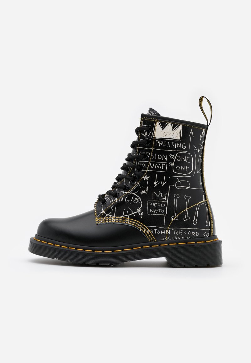 Botte en cuir noir à lacets avec des coutures jaunes et des textes et dessins style graffiti blancs sur la partie supérieure et la zone du talon.