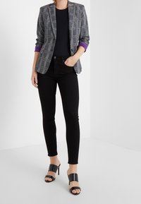 Blazer de cuadros en gris con puños morados, llevado sobre una blusa negra, combinado con jeans skinny negros y sandalias de tacón negro.