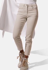Beige geribbelde high-waisted broek met vijf zakken, sluiting met een knoop aan de voorkant en rits, gecombineerd met lichtgekleurde enkellaarsjes.