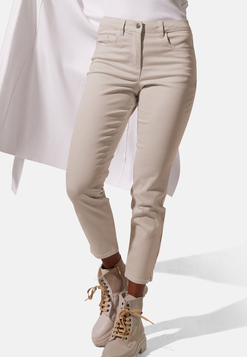 Beige geribbelde high-waisted broek met vijf zakken, sluiting met een knoop aan de voorkant en rits, gecombineerd met lichtgekleurde enkellaarsjes.